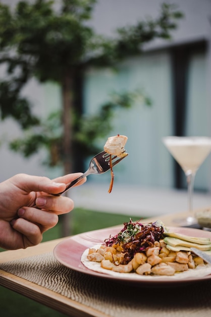 Vertical shot of a person eating a dish with chicken avocado slices and red cabbage