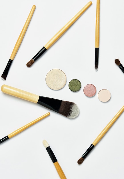 Vertical shot, randomly placed professional makeup brushes, with symmetrically laid nude eye shadow palette, isolated on white background. Top view, flatlay. The concept of makeup, cosmetics, visage.