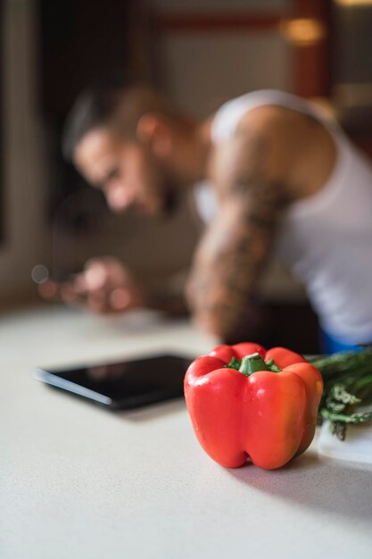 Colpo verticale di un peperone rosso su un tavolo da cucina con un atleta maschile sullo sfondo sfocato