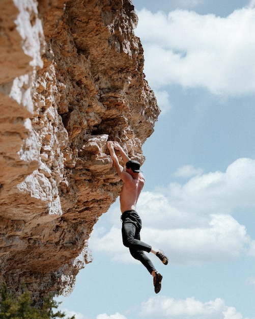 Vertical shot of a shirtless guy rock climbing on a sunny day