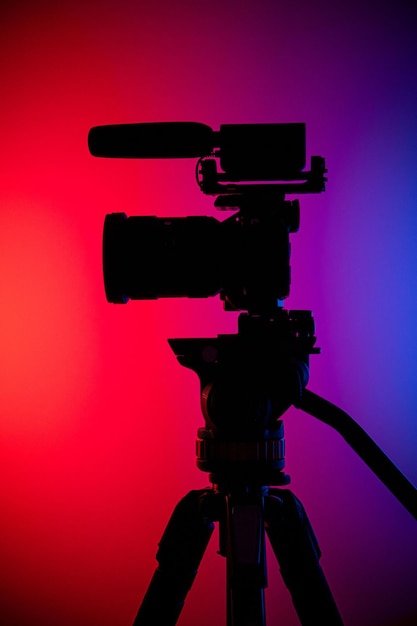 Photo vertical shot of a silhouette of a camera on a tripod against a redpurple gradient background