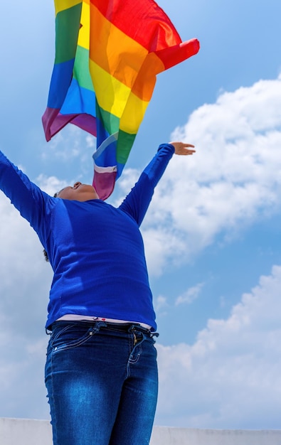 A vertical shot of a small smiling girl throwing a rainbow flag up