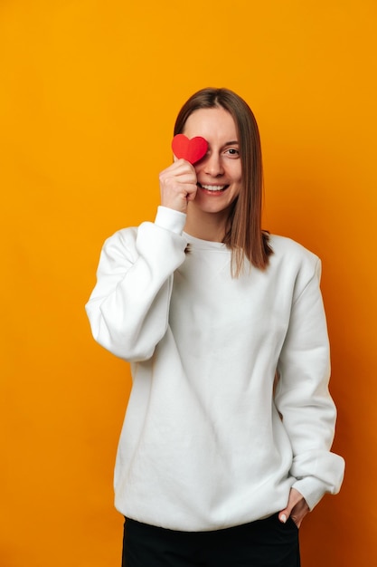 Vertical shot of a smiling young woman covering one eye with a red heart