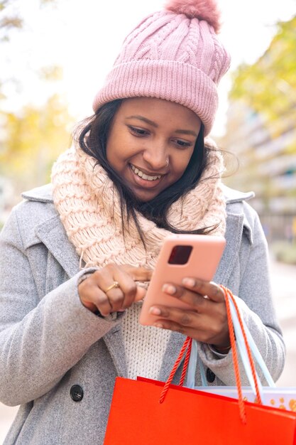 Vertical shot smiling young woman holding shopping bags browsing smartphone apps