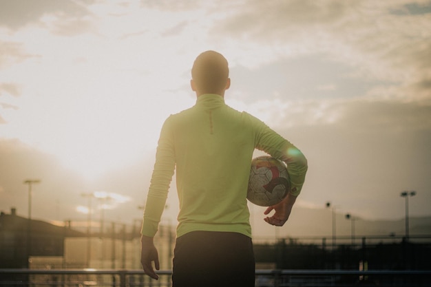 Vertical shot of soccer player with his back turned holding a\
soccer ball.