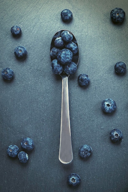 Vertical shot of a spoon with red blueberries on a slate background