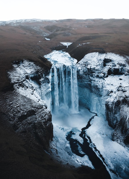 Foto colpo verticale di una cascata e di un fiume ghiacciato che scorre sulle montagne in islanda