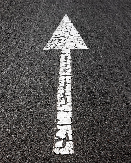 Vertical shot of white arrow sign on asphalt road