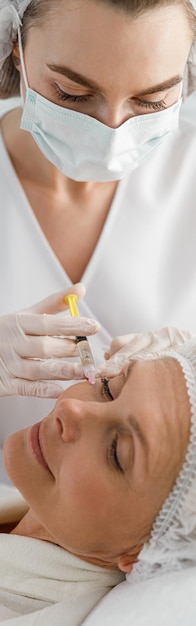 Vertical shot of woman cosmetologist making injection to mature female client in clinic