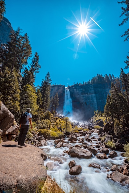 Vertical shot of a woman in front of the waterfall and trees in Yosemite National Park