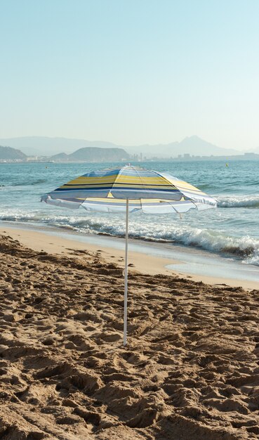 Vertical shot of a yellow and blue striped umbrella on the beach on a sunny day