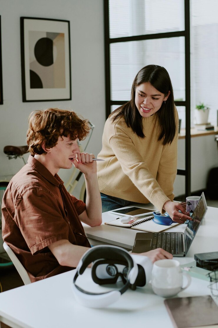 Photo vertical shot of young adult brunette female developer pointing at laptop screen while her coworker