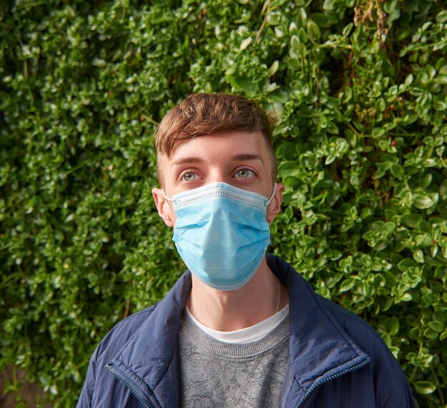 A vertical shot of a young Caucasian guy wearing a sanitary mask outdoors