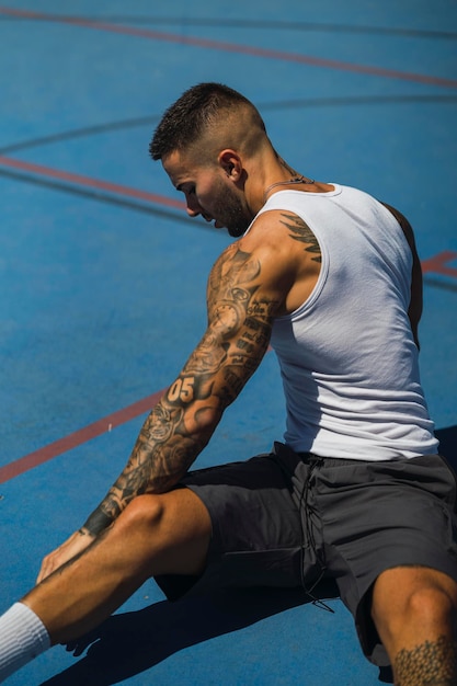 Vertical shot of a young caucasian guy with cool tattoos sitting on the basketball court