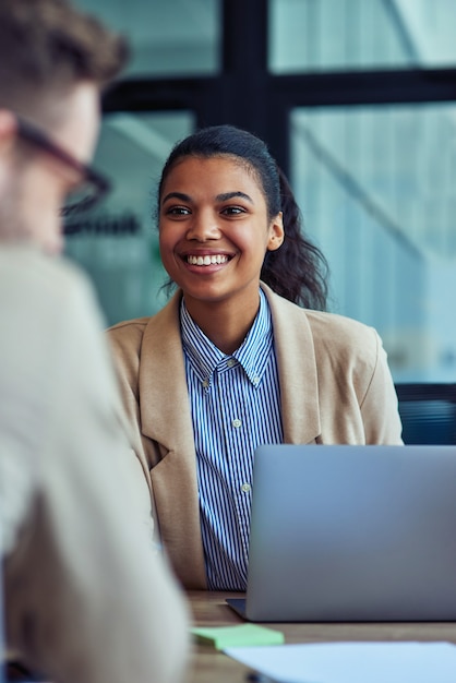 Vertical shot of a young cheerful mixed race female office worker working on laptop in the modern