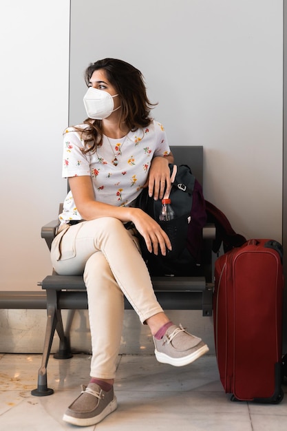 Foto giovane passeggero femminile con ripresa verticale con maschera facciale con borse e bagagli in aeroporto o stazione