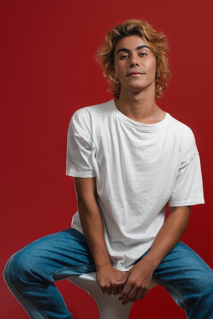 Photo a vertical shot of a young male in a white shirt posing on the background of a red wall