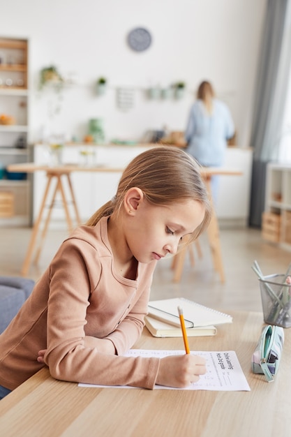 Photo vertical side view portrait of cute girl doing homework for elementary school while studying at home in cozy interior, copy space