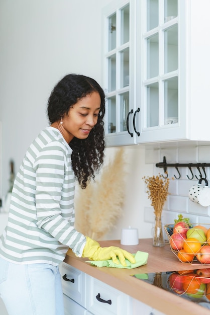 Photo vertical of smiling africanamerican female washing kitchen surface in gloves with washcloth