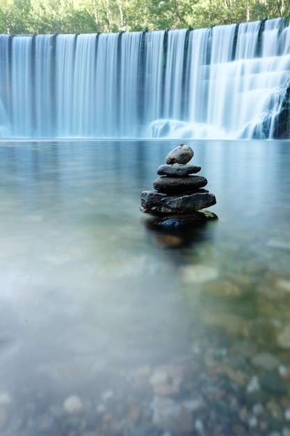 Vertical stones in river and waterfall background