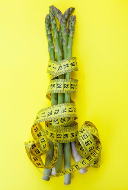 Vertical top view shot of bunch of asparagus with tape measure on yellow background