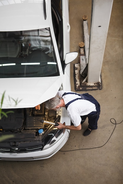 Vertical top view shot of an elderly car servie engineer checking engine of a car at the workshop