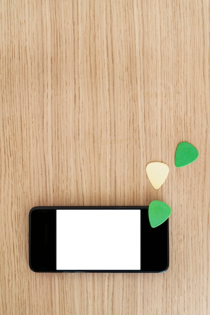 Vertical top view of smartphone screen with blank content.
study and learn guitar lessons online concept. explore music and
technology together. guitar picks and white screen phone copy
space.