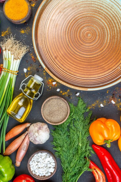 Vertical view of blue plate and fresh vegetables fallen oil bottle spices green bundle