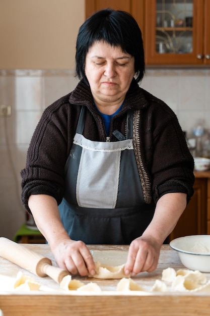 小麦粉ベーカリーの概念を持つ木製のテーブルで生地からパン屋を作るブルネットの女性の垂直方向のビュー