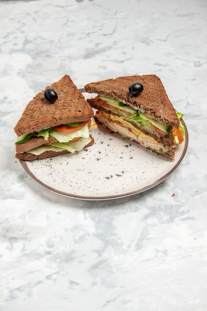 스테인드 흰색 표면에 접시에 올리브로 장식 된 검은 빵과 함께 맛있는 샌드위치의 세로보기