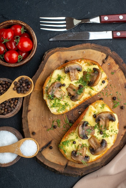 Vista verticale di uno spuntino delizioso con funghi su tavola di legno e posate pomodori al pepe su sfondo nero