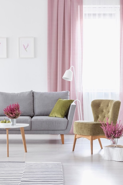 Vertical view of elegant living room with grey comfortable couch olive green armchair and heather in metal pots real photo