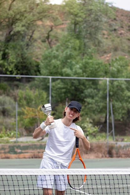 Photo vertical view of excited young teenager pointing his new champion winning cup holded on his hand