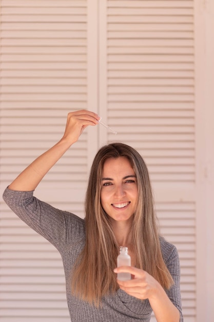 Vertical view of happy young woman with blond hair putting anti hair loss serum on hair in fall time