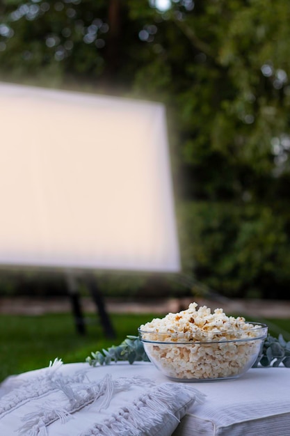 Vertical view of isolated popcorn bowl and a projector screen in the background playing a movie in the park at night