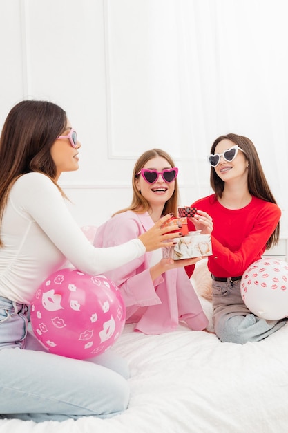 Photo vertical view of the overjoyed beautiful girls best friends wearing sunglasses holding gifts