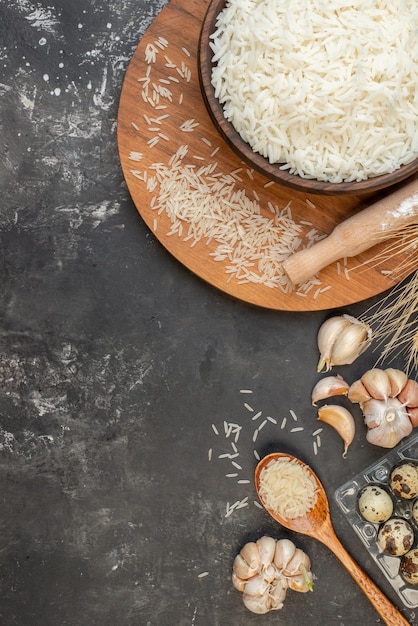 Vertical view of perfect long rice in brown pot and on wooden board garlic eggs spoon on gray background