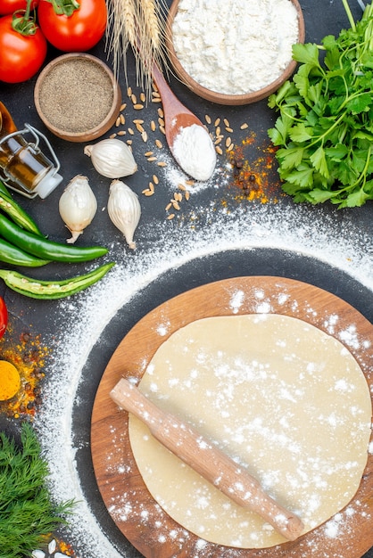 Vertical view of rolling pin over the circle dough on wooden board and set of foods