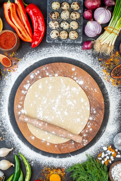 Vertical view of rolling pin over the circle dough on wooden cutting board and set of foods