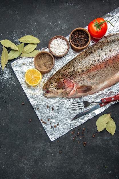 Vista verticale delle squame rimosse posate di pesce fresco set di foglie di alloro pomodoro e spezie diverse su sfondo di colore scuro