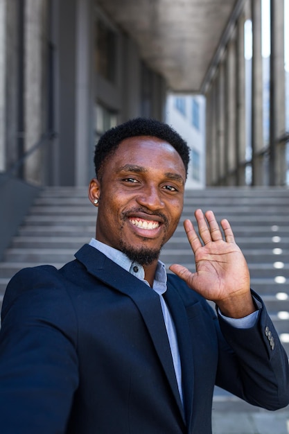 Vertical view smartphone camera african american businessman\
speaks on phone using a front camera on a video call. black\
business man talking on webcam. conversation of an office worker in\
suit