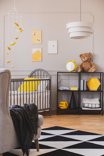 Vertical view of stylish grey and yellow baby bedroom with crib and industrial black metal shelf