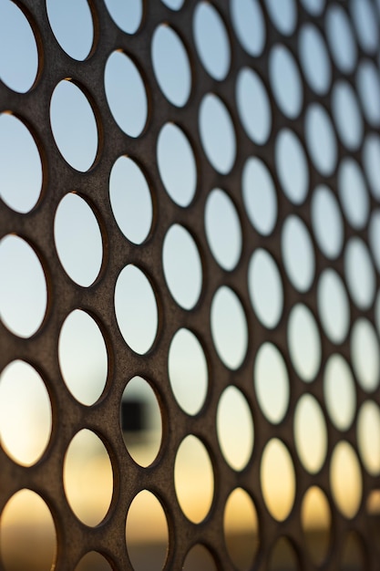Vertical view of the sunset through a perforated steel sheet with holes in the shape of circles Selective focus