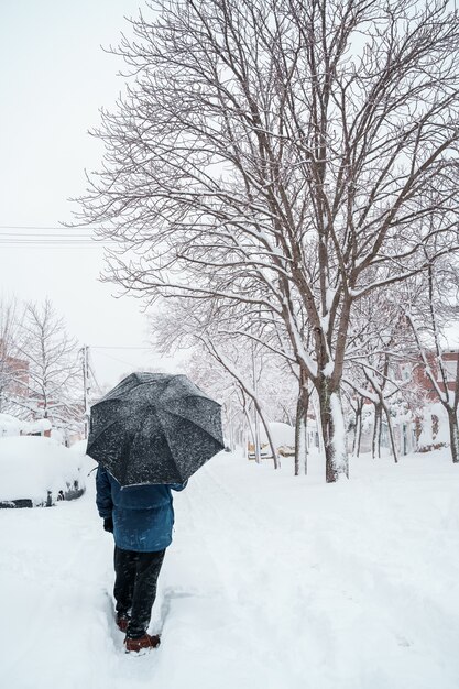 Vertical view of unrecognizable traveler with an umbrella in the middle of the snow.