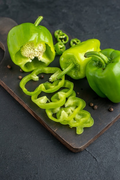 Vertical view of whole cut chopped green peppers on dark color wooden cutting board on black surface