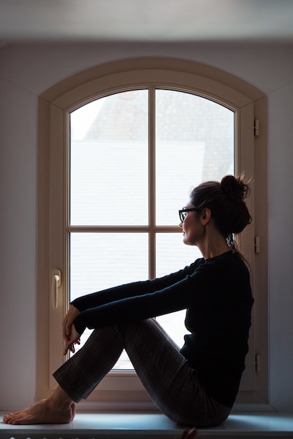 Vertical view of woman worried looking through the window at home.