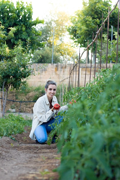 Vertical view of young blonde woman happy with her ecologic tomato in hand