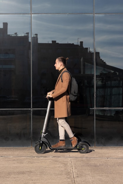 Вертикальный вид молодого бизнесмена, едущего на электрическом скутере по финансовому району центра города