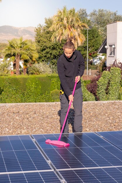 Vertical view of young man cleaning with a mop the solar panels of his house in the roof of it