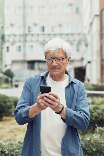 Ritratto verticale in vita di un uomo anziano moderno che utilizza lo smartphone all'aperto ambiente accogliente della città, spazio di copia